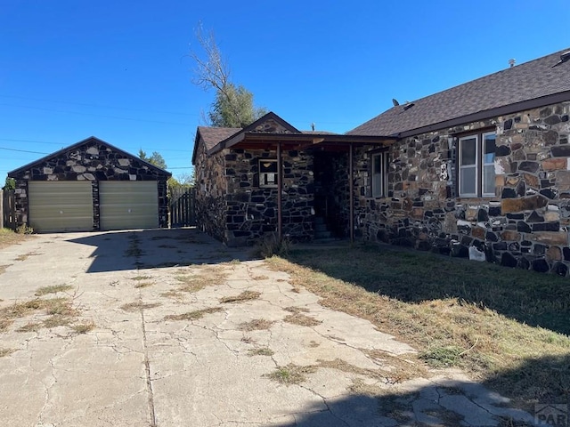 ranch-style home with a shingled roof, an outbuilding, stone siding, and a detached garage