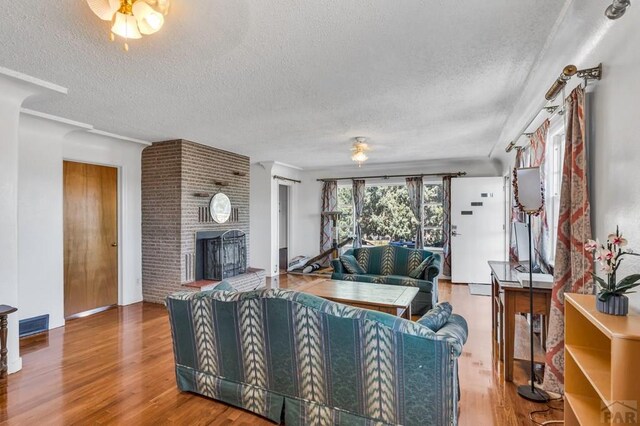 living room featuring a brick fireplace, a textured ceiling, and wood finished floors