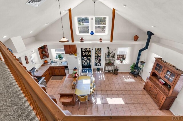 dining room with a wood stove, light tile patterned floors, visible vents, and high vaulted ceiling