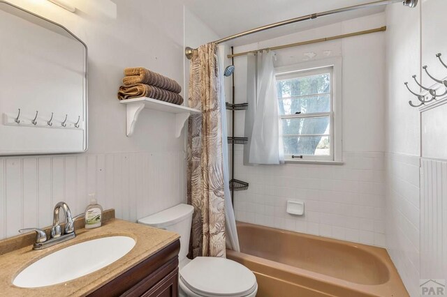 full bath featuring a wainscoted wall, toilet, shower / bath combination with curtain, and vanity