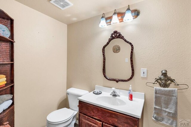 half bathroom featuring visible vents, vanity, and toilet