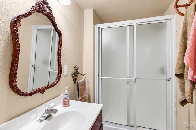 full bath featuring a textured wall, a shower with door, and vanity