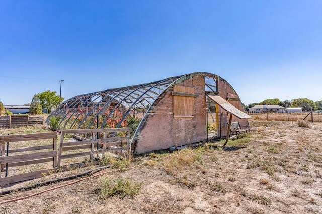 view of outdoor structure with a rural view, an outdoor structure, and fence