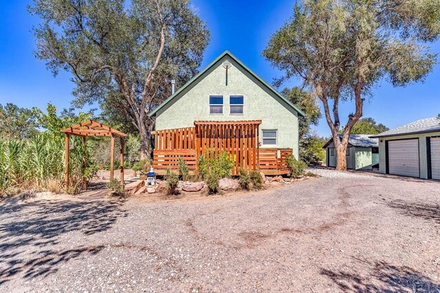 view of front of property with a garage, driveway, an outbuilding, a wooden deck, and stucco siding