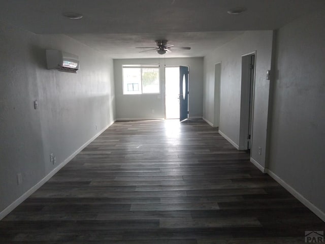 spare room featuring dark wood-type flooring, a wall unit AC, baseboards, and a ceiling fan