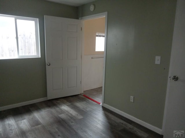 empty room featuring dark wood-style flooring, plenty of natural light, and baseboards