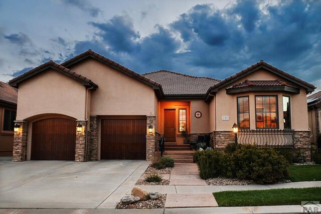 view of front facade featuring a tile roof, stucco siding, concrete driveway, an attached garage, and stone siding