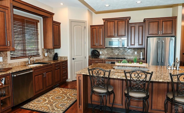 kitchen with light stone counters, appliances with stainless steel finishes, a kitchen island, a sink, and a kitchen bar