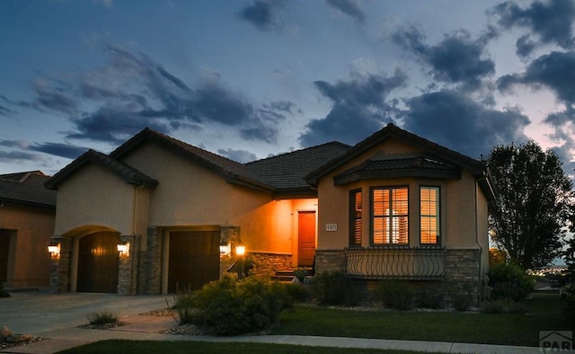 view of front facade with a tile roof, stucco siding, an attached garage, stone siding, and driveway