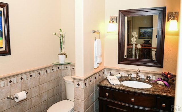 half bathroom with tile walls, wainscoting, vanity, and toilet