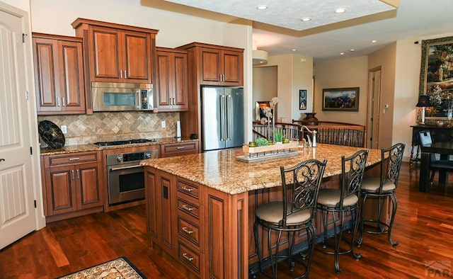 kitchen with dark wood-style floors, stainless steel appliances, tasteful backsplash, an island with sink, and a kitchen bar