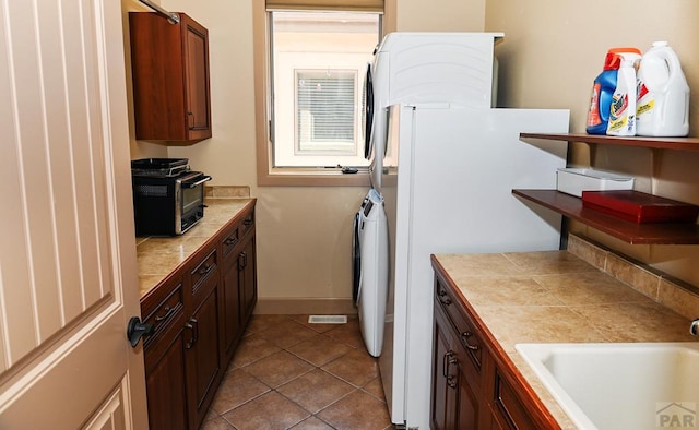 kitchen featuring light tile patterned floors, a toaster, a sink, freestanding refrigerator, and tile counters