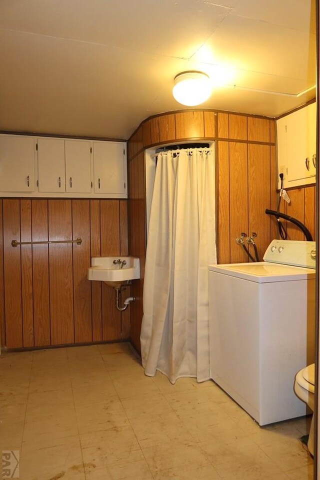 washroom with laundry area, wood walls, a sink, and washer / dryer