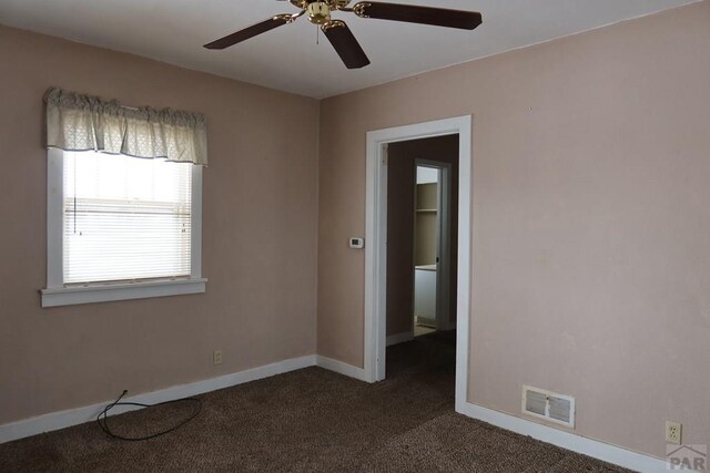 empty room featuring ceiling fan, dark carpet, visible vents, and baseboards