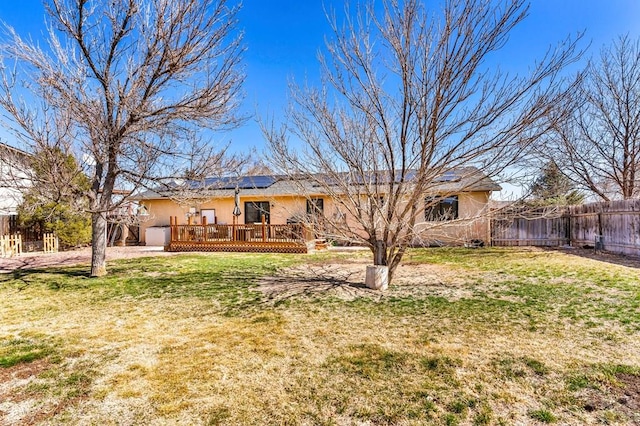 rear view of property with fence, roof mounted solar panels, stucco siding, a deck, and a yard