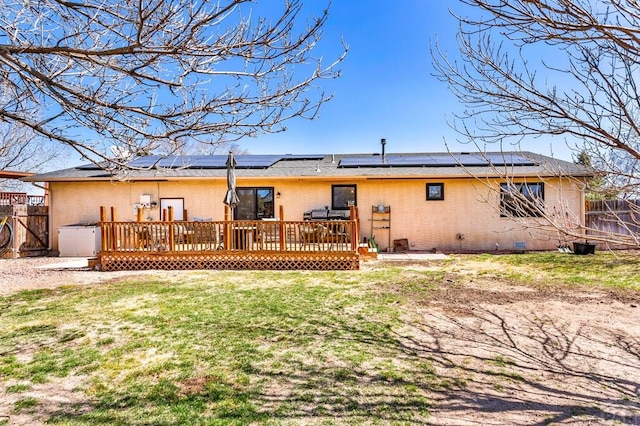 back of property with brick siding, a deck, a yard, and fence