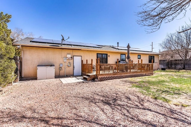 rear view of property featuring brick siding, solar panels, a deck, and fence