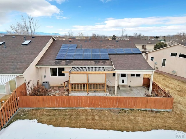 rear view of house with a fenced backyard, solar panels, a shingled roof, stucco siding, and a patio area