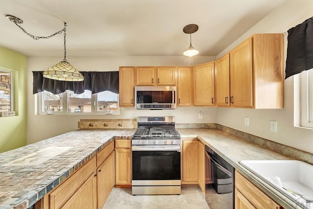 kitchen with appliances with stainless steel finishes, light brown cabinets, a peninsula, and decorative light fixtures