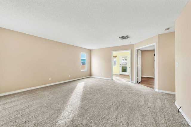 spare room featuring carpet floors, visible vents, a textured ceiling, and baseboards