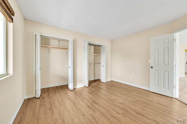 unfurnished bedroom featuring light wood finished floors, a textured ceiling, baseboards, and multiple closets