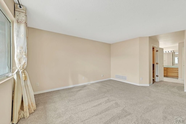 unfurnished bedroom featuring carpet floors, visible vents, ensuite bath, and baseboards