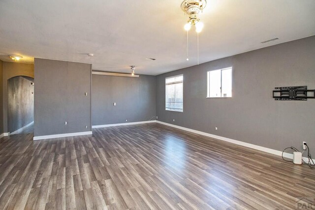 empty room with arched walkways, visible vents, baseboards, and wood finished floors