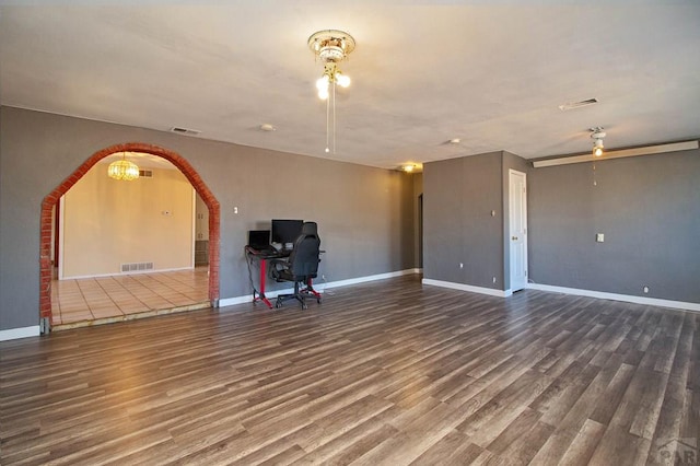 unfurnished living room with arched walkways, visible vents, and wood finished floors