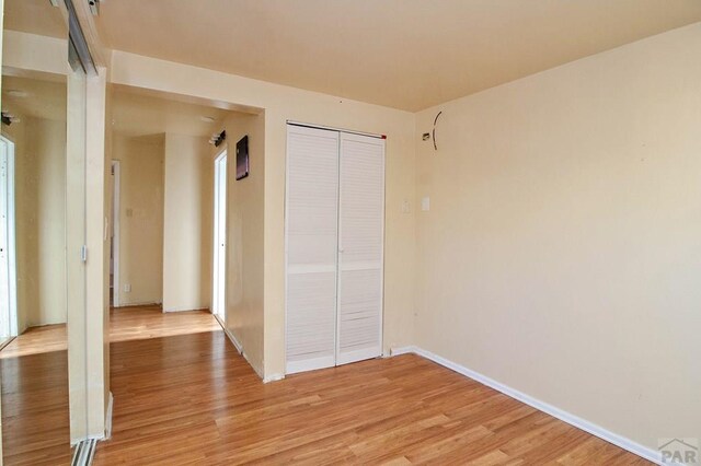 unfurnished bedroom featuring light wood-type flooring, a closet, and baseboards