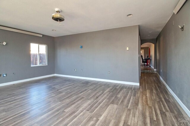 empty room with baseboards, arched walkways, and dark wood-type flooring