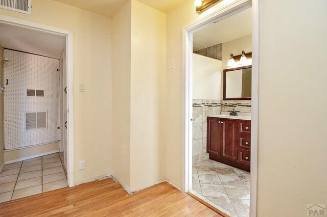 hallway featuring light wood-style floors, visible vents, and a sink