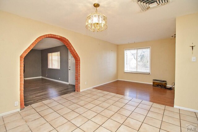 unfurnished room with arched walkways, visible vents, an inviting chandelier, light wood-style floors, and baseboards