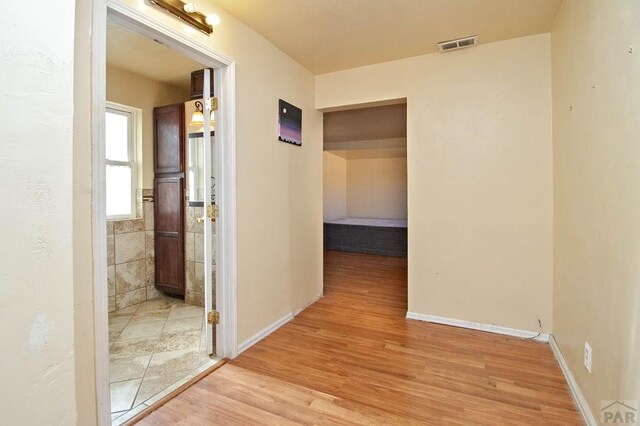 corridor with light wood-type flooring, baseboards, and visible vents