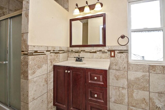 full bath featuring a wainscoted wall, a shower with door, vanity, and tile walls