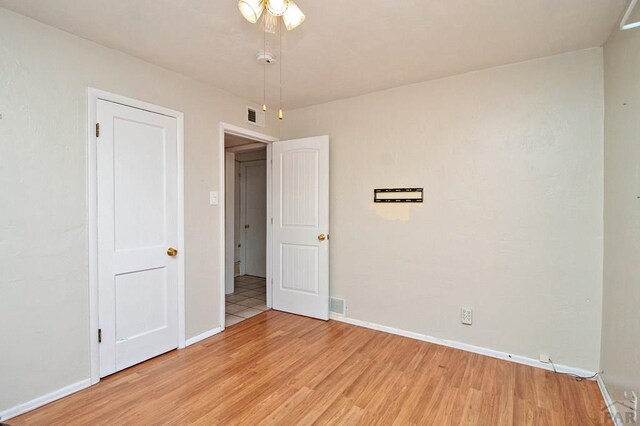 empty room with light wood-type flooring, visible vents, and baseboards