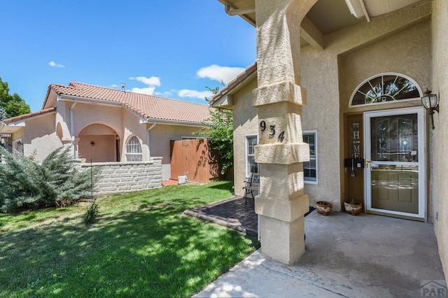 doorway to property with a tile roof, a lawn, and stucco siding