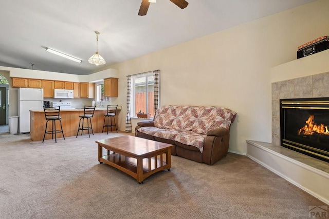 living area with a ceiling fan, a tiled fireplace, and light colored carpet