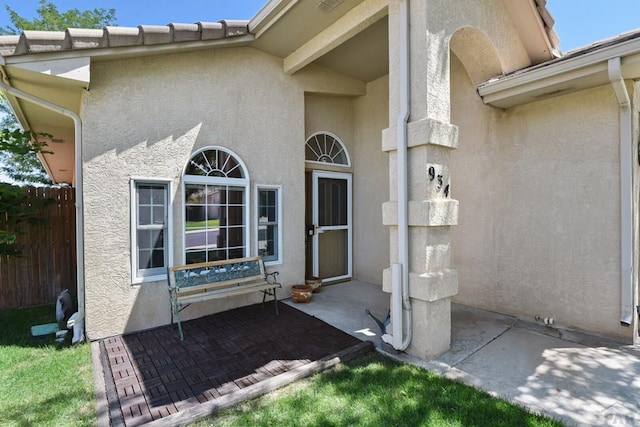 view of exterior entry with fence and stucco siding