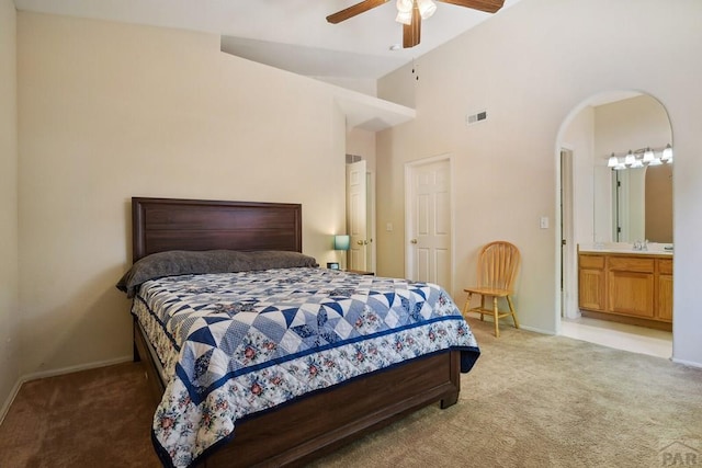 bedroom featuring light carpet, visible vents, arched walkways, and connected bathroom