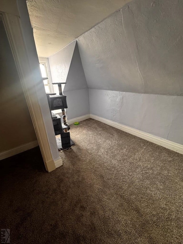 additional living space with lofted ceiling, dark colored carpet, a textured ceiling, and baseboards