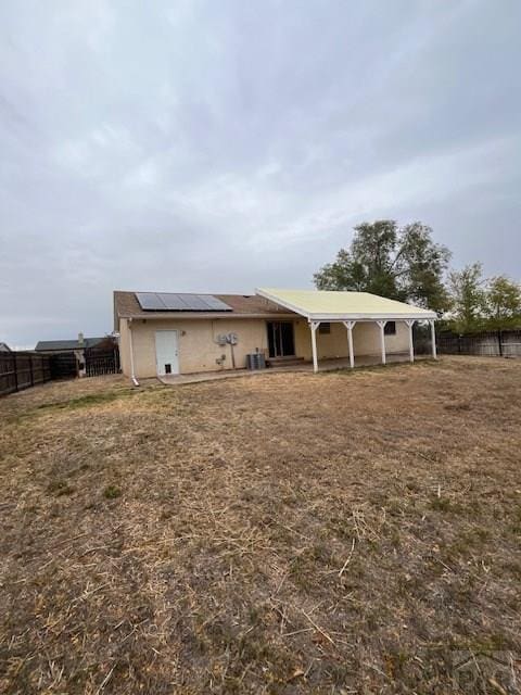 back of property with solar panels, central AC, and a fenced backyard