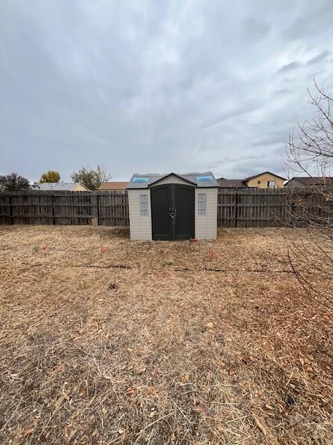 view of yard featuring a storage shed, a fenced backyard, and an outdoor structure