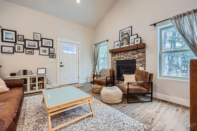 living room with high vaulted ceiling, a fireplace, baseboards, and wood finished floors