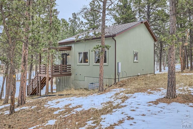 view of snowy exterior featuring stairs, a wooden deck, and stucco siding