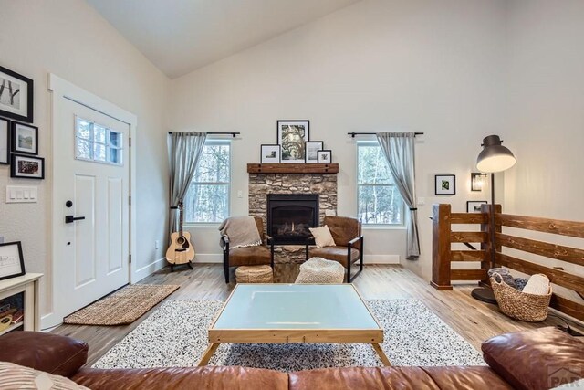 living area with high vaulted ceiling, a healthy amount of sunlight, a fireplace, and light wood finished floors