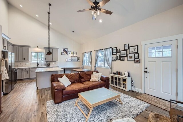 living area with high vaulted ceiling, recessed lighting, a ceiling fan, and light wood-style floors