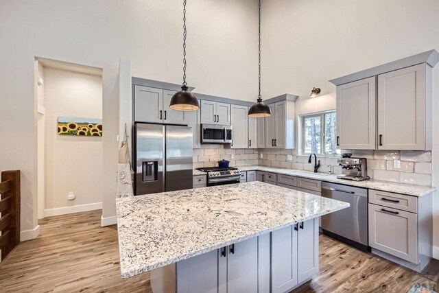 kitchen featuring a center island, appliances with stainless steel finishes, light stone counters, and decorative light fixtures