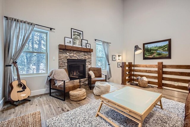 living area with a stone fireplace, wood finished floors, a high ceiling, and a healthy amount of sunlight