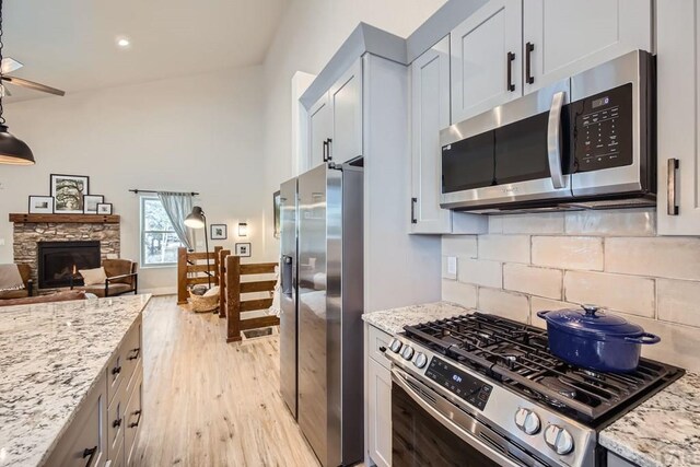 kitchen featuring light wood finished floors, a stone fireplace, appliances with stainless steel finishes, and light stone counters