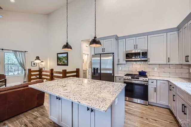 kitchen featuring a kitchen island, appliances with stainless steel finishes, light stone counters, high vaulted ceiling, and pendant lighting